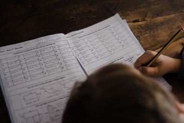 A child writes in a workbook using a pencil.