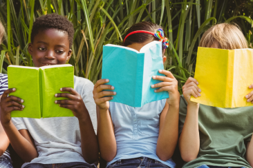 Children sitting in a row holding books in front of their faces