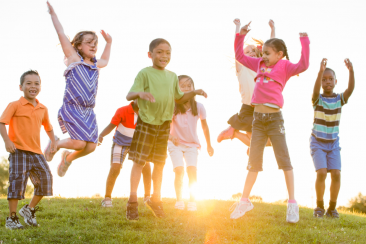 Colour photo of children jumping on some grass with sun shining behind them