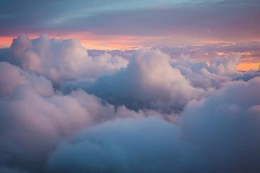 A view from an aeroplane of puffy white clouds with a sunset in the background