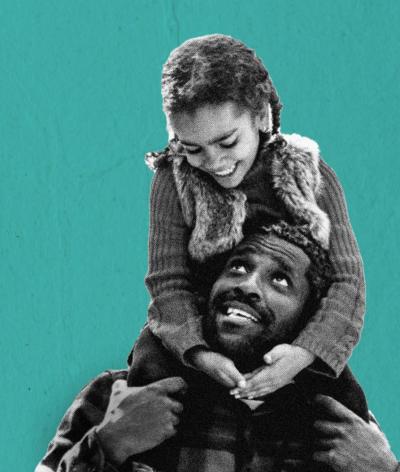 A daughter sitting on her father's shoulders, against a teal backdrop