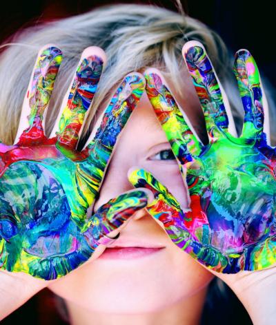 Boy covering his face with hands covered in multicolor paint