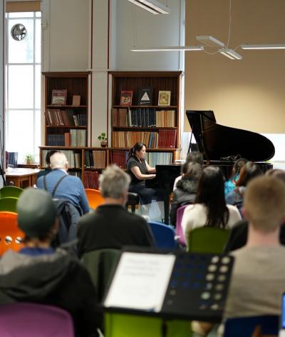 A pianist on a grand piano performing to a crowd in a library