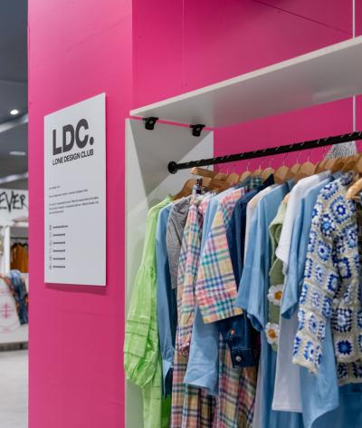 A rail of colourful clothes against a bright pink pillar in the pop up at 500 Oxford Street
