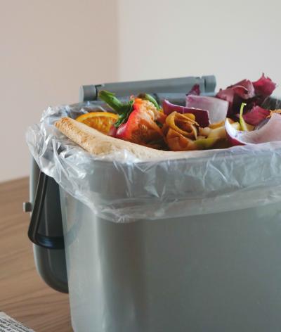 A silver food waste bin, with a plastic liner and full of vegetable peelings, stale bread and teabags