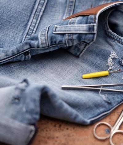 Colour photo of jeans being repaired with thread, pins and needles