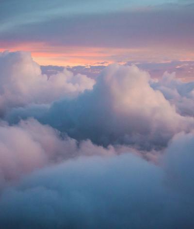 A view from an aeroplane of puffy white clouds with a sunset in the background