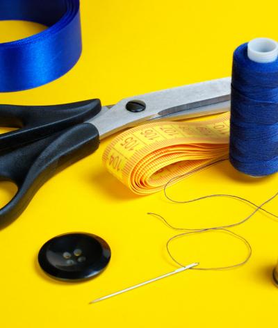 Colour photo of ribbon, scissors, measuring tape, thread, button, needle and thimble