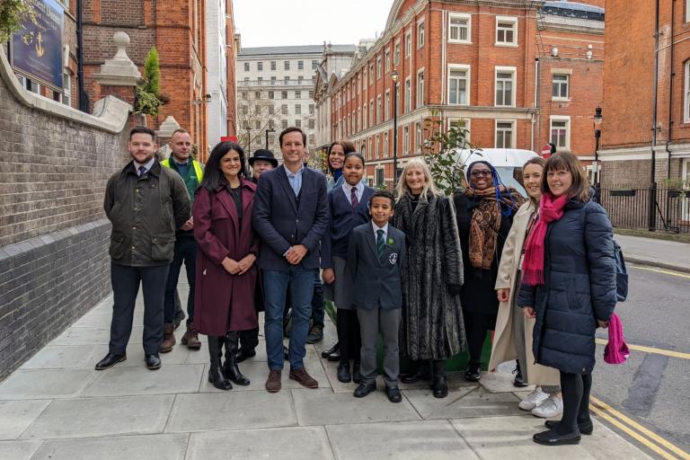 A group of school children and teachers as well as a Westminster councillor are outside standing together and smiling to the camera at the launch of the a new small park