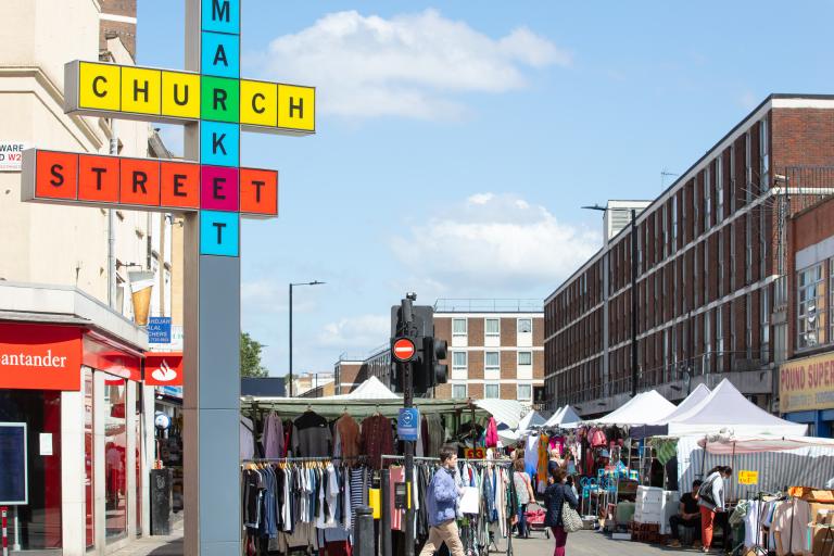 The entrance to church street market on a sunny day with the red blue and yellow sign that reads 'Church Street Market' on the left hand side