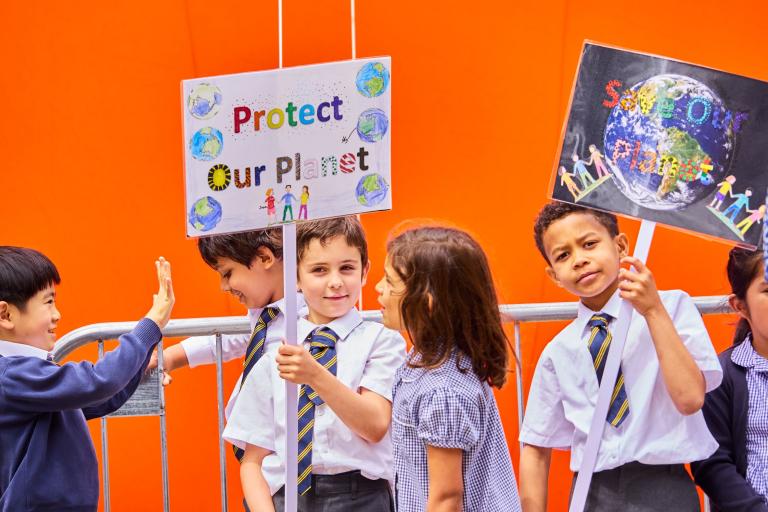 A group of children standing in front of an illustrative one tonne bubble of CO2 with signs that say 'Protect our planet' and 'save our planet'