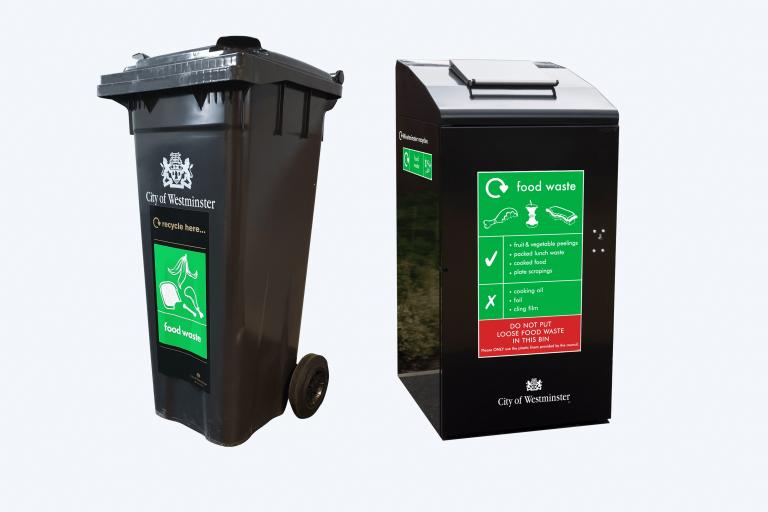 A fixed black outdoor food waste bin and a black wheelie bin, both with a green sign on the front saying what food waste can and can't be recycled.