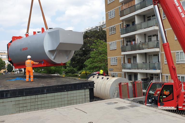 A new large boiler being installed by a crane on a housing estate