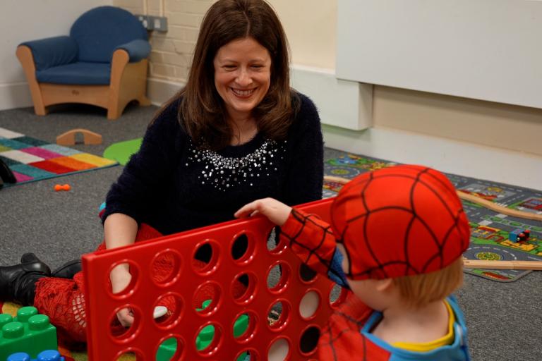 Woman playing connect 4 with young boy wearing a spider man costume 