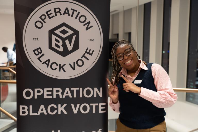 A delegate standing beside an Operation Black Vote banner