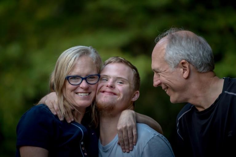 Happy picture of a teenager with down syndrome hugging a woman and a man.jpg
