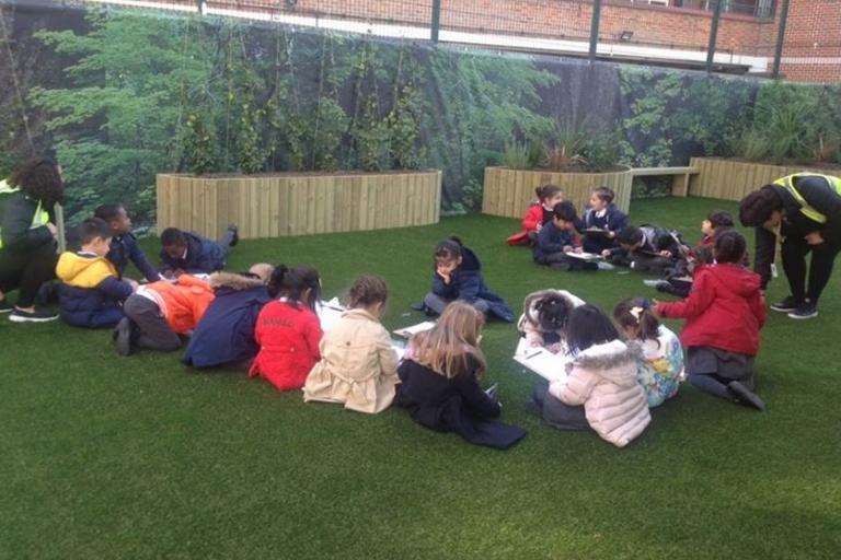 Kids sitting on the grass and drawing in a school garden