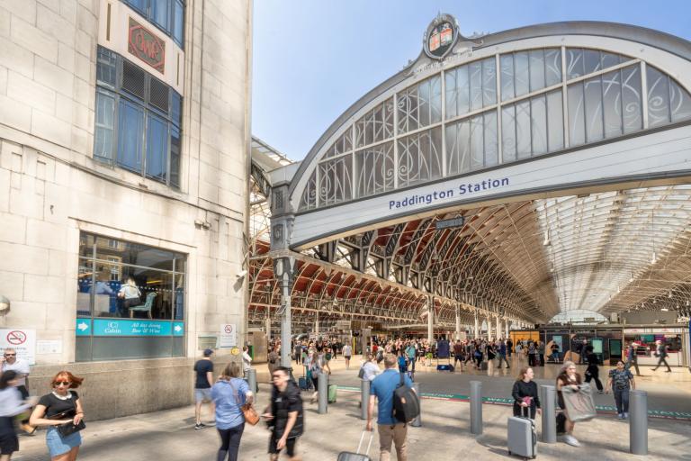 The outside of paddington station with people coming and going through the arched glass entrance