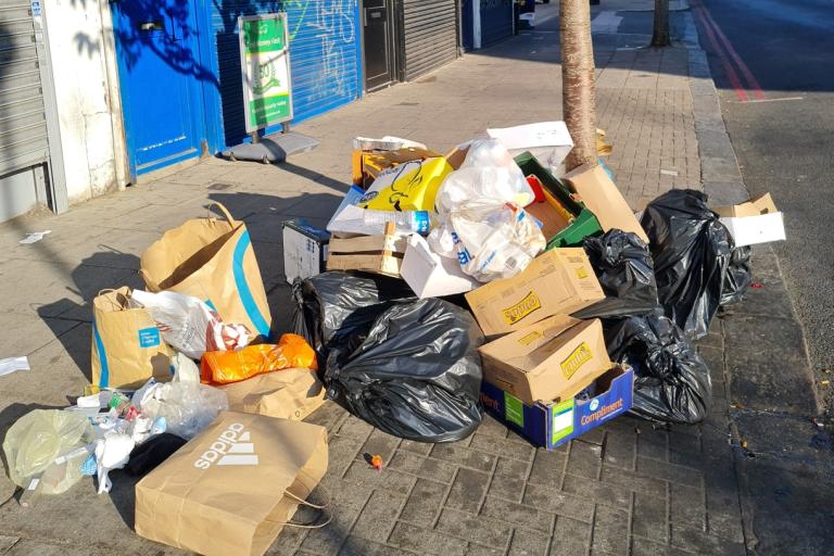 A pile of overflowing cardboard boxes, black bin bags and rubbish blocking the pavement 