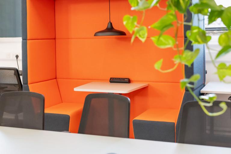 A desk and a bright orange seating booth with a light and plugs.