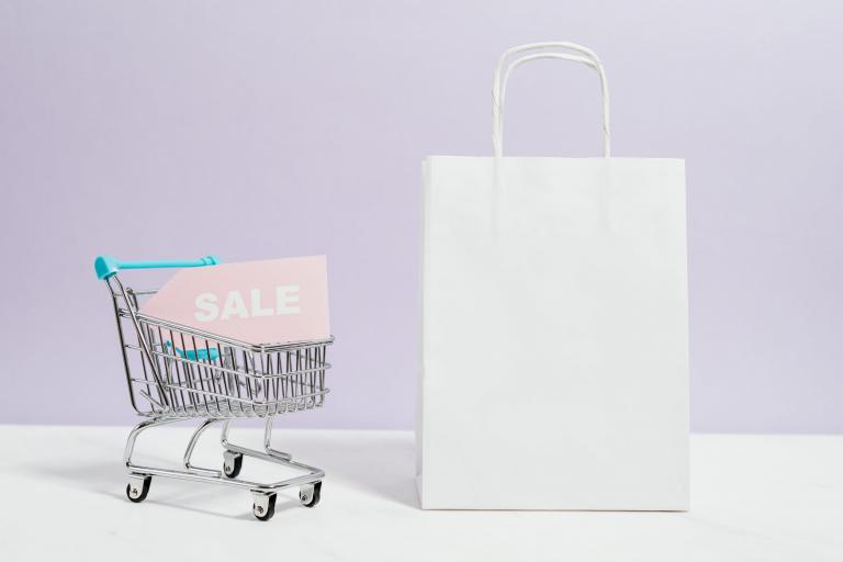 White paper bag and mini trolley with a pink sale sign