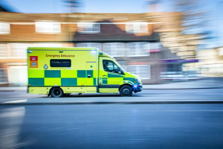 An ambulance driving down a street. The houses in the background is blurred to give the feeling of movement.