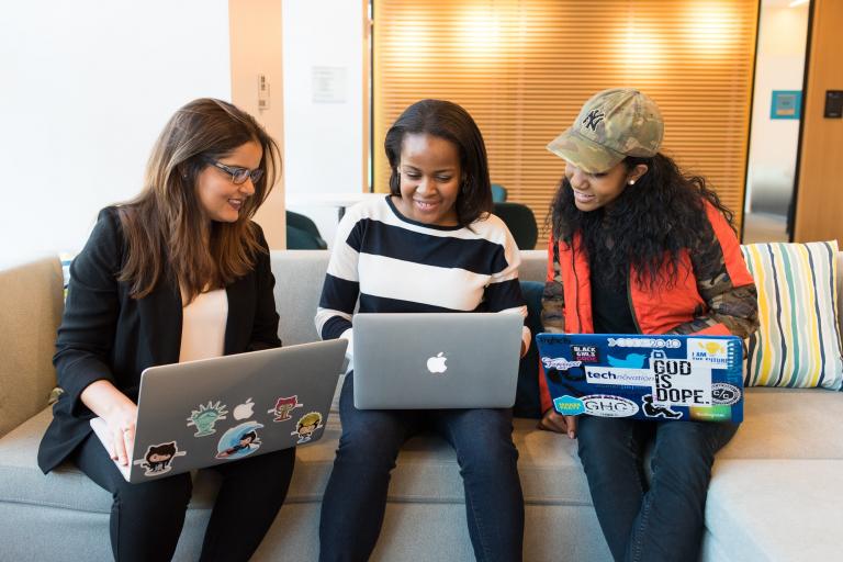 Colour photo of 3 women sitting on a sofa looking at their laptops 