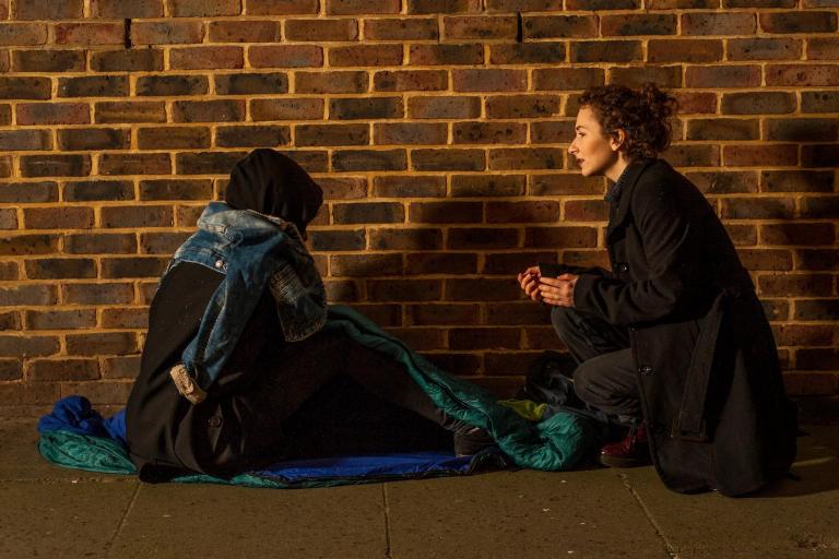 Image of a homeless man sitting on the ground talking to a support worker 
