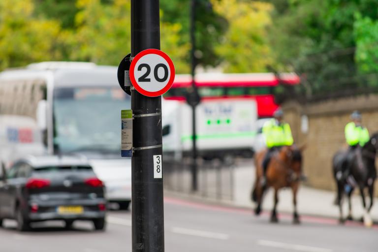 A 20 miles per hour sign on a Westminster street with two police horses in the background