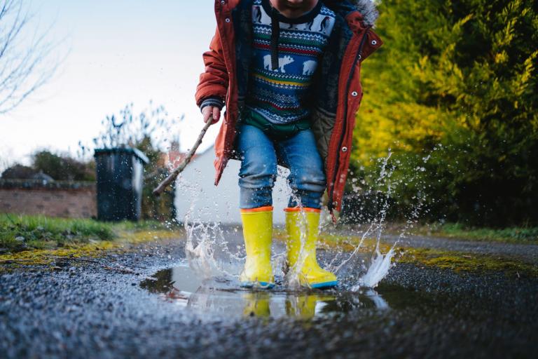 Child in Christmas jumper splashing in puddle