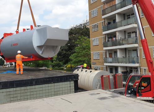 A new large boiler being installed by a crane on a housing estate