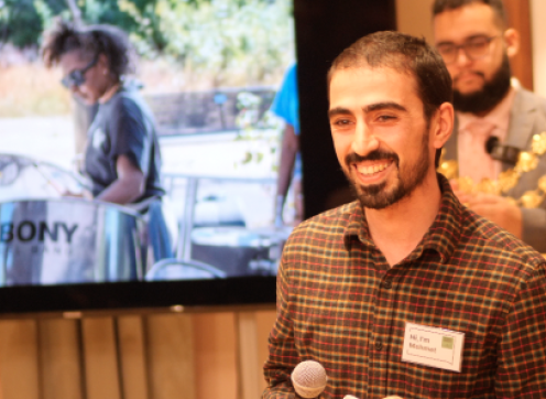 Mehmet at an event where he was sharing his volunteering story, he's holding a mic and standing at the front of a room