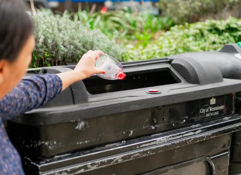 A woman putting a plastic bottle into a Westminster recycling bin