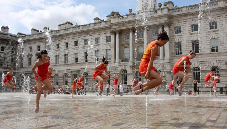 Woman in orange dancing outside Summerset House, in the fountain