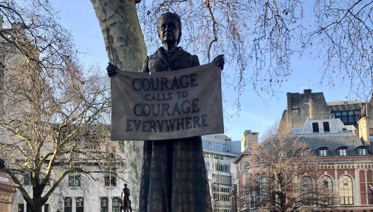 Image of a statue holding up a sign saying 'courage calls, to courage everywhere'