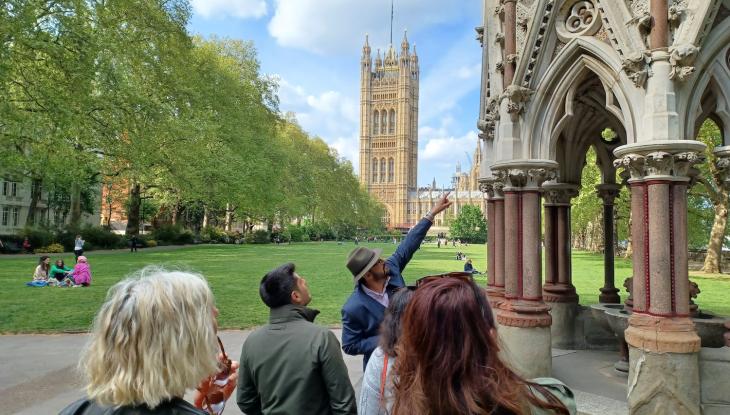 Image of a group of people in a park lead by a tour guide pointing upwards.